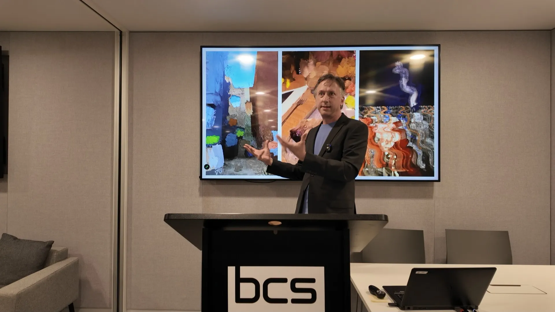 Alex May speaking at the BCS lectern in front of projected artworks during Move Fast and Break Things