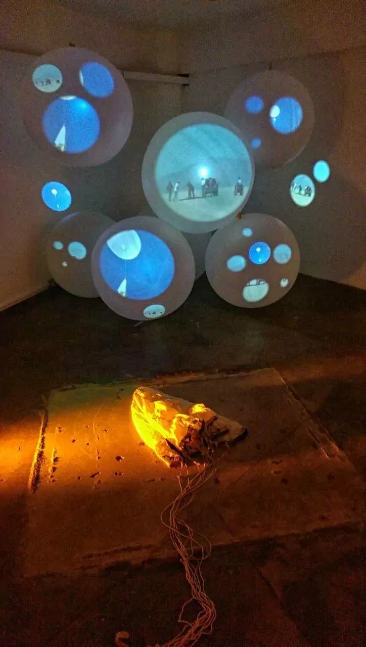 Projected launch footage appears across suspended weather balloons above a collapsed parachute in Fallen Angel.