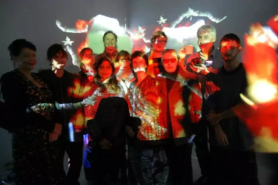 Workshop participants stand together while projected moving image maps across their bodies and the gallery wall in Painting With Light: Video Sculptures.