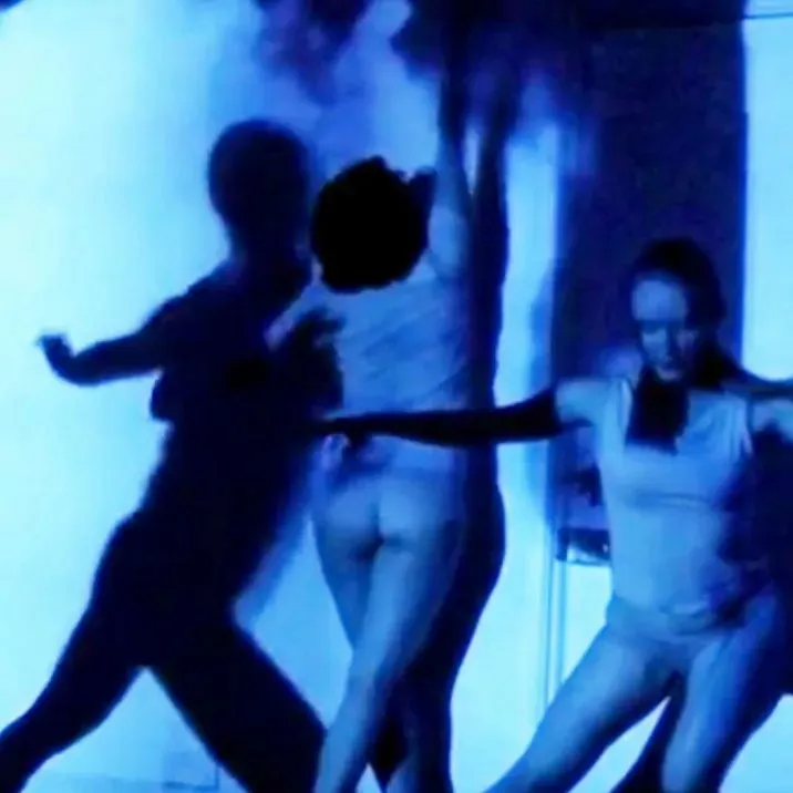 Performance still from Monotone Symphony showing projected light interacting with dancers in a dark gallery space.